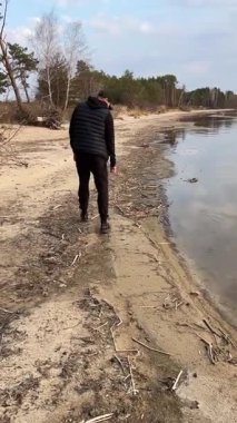 Issız bir sahilde dramatik bulutlu bir gökyüzü altında yürüyen bir adamın arka görüntüsü. Huzurlu doğa manzarası. Bahar ya da kışın nehir kenarında. Dikkatli yürüyüş ve huzurlu anlar