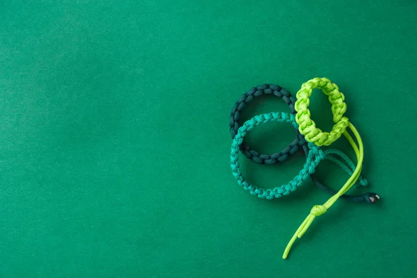 Three simple green paracord bracelets placed on a green grainy p