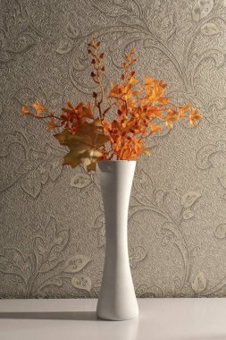 Masadaki vazoda yapay dekoratif dallar ve akçaağaç yaprağı.