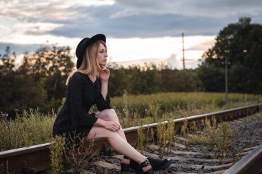 Demiryolunda oturan, elbise ve şapkalı çekici bir kadın.