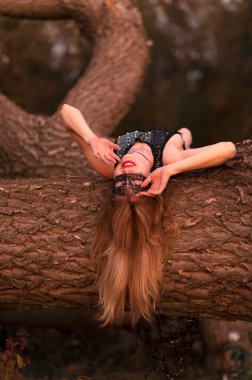 Maskeli genç bir kadın ormandaki bir ağaçta yatıyor.
