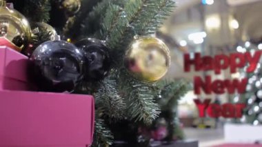 Mutlu Yıllar 'ın üç boyutlu harfleri altın ve siyah toplarla süslenmiş bir Noel ağacının arka planına doğru ilerler.
