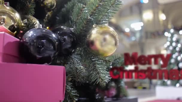 Letras tridimensionais do Feliz Natal movem-se para a frente contra o fundo de uma árvore de Natal decorada com bolas douradas e pretas — Vídeo de Stock