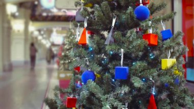 Parlak geometrik oyuncaklarla süslenmiş Noel ağacı GUM alışveriş merkezinin koridorunda duruyor. Ziyaretçiler bulanıklaşıyor