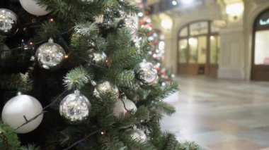 GUM 'da gümüş toplarla süslenmiş bir Noel ağacının arkasında yürüyen ziyaretçilerin videosu.