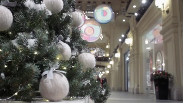 Ένα χριστουγεννιάτικο δέντρο διακοσμημένο με μάλλινες μπάλες από νήμα στέκεται στο λόμπι ενός εμπορικού κέντρου με φόντο τις βιτρίνες των καταστημάτων. — Αρχείο Βίντεο