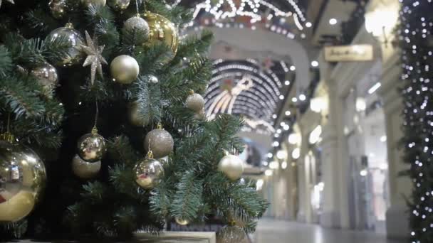 Uma árvore de Natal decorada com bolas de ouro fica no átrio do centro comercial contra o fundo das janelas da loja. — Vídeo de Stock