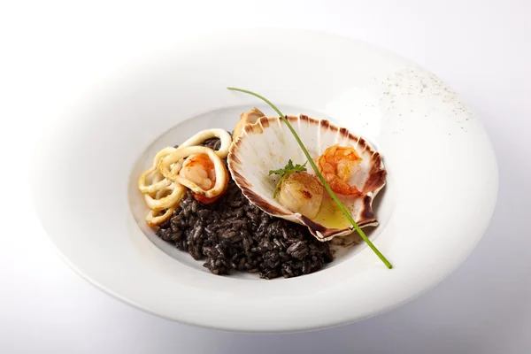 Czarne risotto z owocami morza serwowane w muszla na białym tle — Zdjęcie stockowe