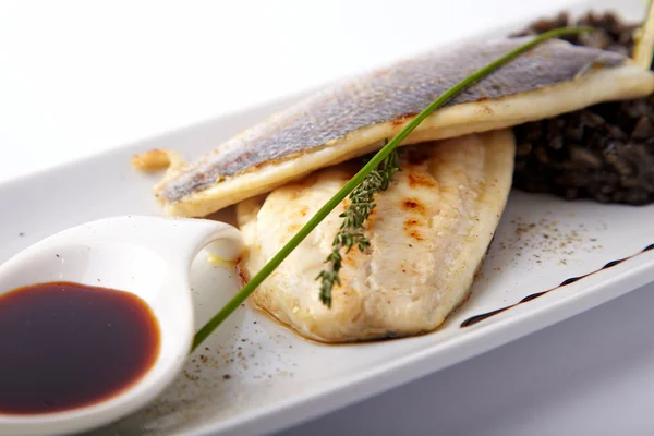 Grilled fish with black risotto on a white background Royalty Free Stock Photos