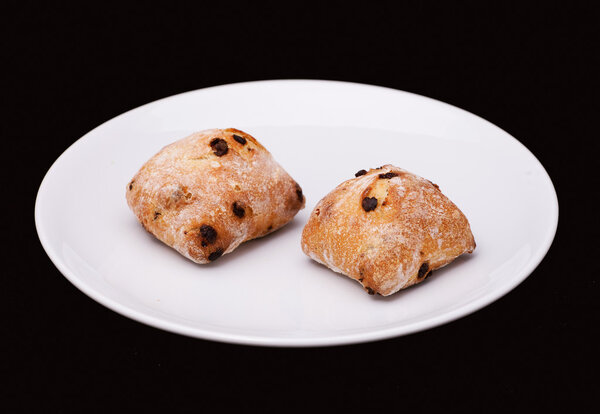 Две булочки с изюмом на белой тарелке

