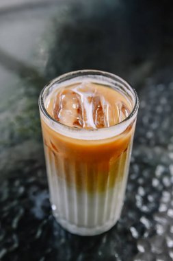 Koyu bir masada espresso, süt ve buz katmanlı buzlu kahve, ferahlatıcı ve soğuk bir içecek.