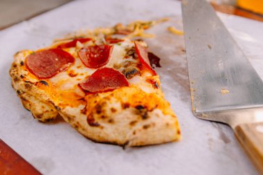 Lezzetli bir pepperoni pizza diliminin spatula tarafından kaldırılmasının yakın çekimi, tatmin edici bir peynir çekme ve çıtır çıtır