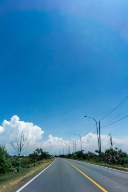Kıvrımlı asfalt yol, parlak mavi gökyüzü ve büyük bulutların altında sokak lambalarıyla kaplı. Seyahatin sembolü, geleceğin yolu, büyüme ve ulaşım