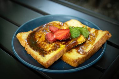 Çilek ve nane ile süslenmiş tatlı şurupla kaplı altın sarısı Fransız tostu dilimleri.