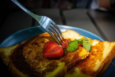 Taze çilek kesen bir çatal. Altın Fransız tostu dilimleri üzerine. Şerbetle serpiştirilmiş, koyu tabakta.