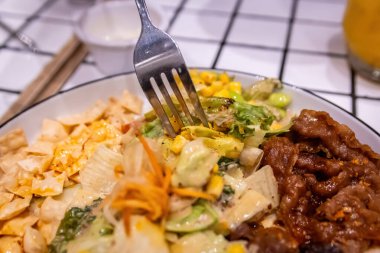 Sağlıklı bir füzyon yemeğinden taze salata ve mısırdan bir ısırık alan bir çatalın yakın çekimi.