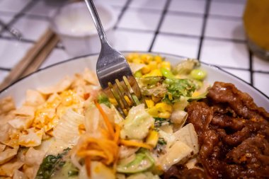 Sağlıklı bir füzyon yemeğinden taze salata ve mısırdan bir ısırık alan bir çatalın yakın çekimi.