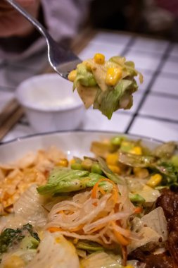 Kremalı sosla kaplı taze salata ve mısırı kaldıran bir çatalın makro görüntüsü..