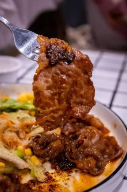 Arka planda salata ve sos kalıntıları olan bir çatal tarafından toplanan bir et parçasının makro çekimi..