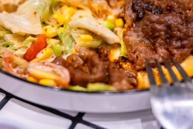 Modern bir tabakta lezzetli bir bifteğe ve taze karışık salataya dokunan çatal. Füzyon yemek detayı