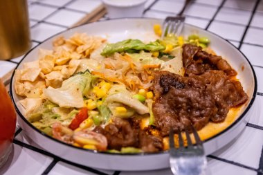 Modern bir tabakta lezzetli bir bifteğe ve taze karışık salataya dokunan çatal. Füzyon yemek detayı