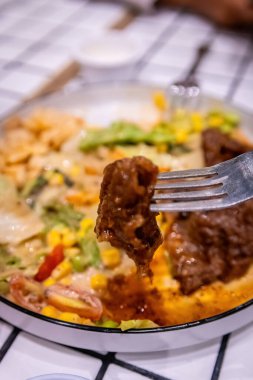 Arka planda salata ve sos kalıntıları olan bir çatal tarafından toplanan bir et parçasının makro çekimi..