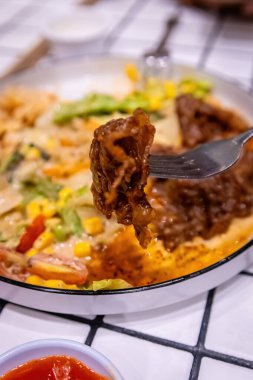 Arka planda salata ve sos kalıntıları olan bir çatal tarafından toplanan bir et parçasının makro çekimi..