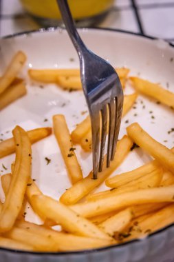 Son baharatlı patates kızartmasını görünen kırıntılarla birlikte beyaz bir tabakta toplayan bir çatalın yakın çekimi.