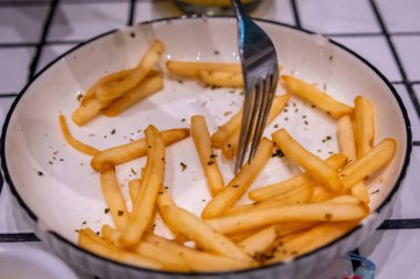 Son baharatlı patates kızartmasını görünen kırıntılarla birlikte beyaz bir tabakta toplayan bir çatalın yakın çekimi.