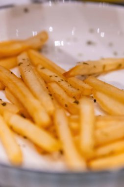 Patates kızartmasının altın dokusunu ve beyaz bir tabakta serpiştirilmiş kuru otları gösteren aşırı yakın çekim makro çekim.