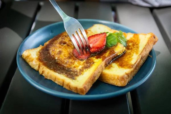 Taze çilek kesen bir çatal. Altın Fransız tostu dilimleri üzerine. Şerbetle serpiştirilmiş, koyu tabakta.