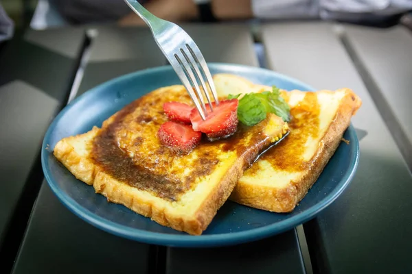 Taze çilek kesen bir çatal. Altın Fransız tostu dilimleri üzerine. Şerbetle serpiştirilmiş, koyu tabakta.
