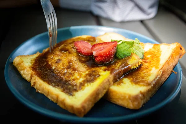 Taze çilek kesen bir çatal. Altın Fransız tostu dilimleri üzerine. Şerbetle serpiştirilmiş, koyu tabakta.