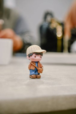 Sade bir arka planda şapka ve kahverengi ceket giyen sevimli minyatür bir erkek figürü.
