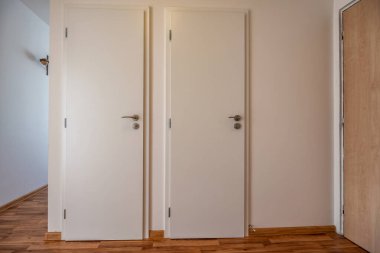 Kapalı iki beyaz ahşap kapılı bir koridor manzarası ve kaplamalı döşeme.