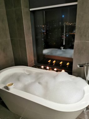Pencerenin yanında köpük banyosu. Mum ışığında, banyoda romantik bir akşam. Spa tedavileri.