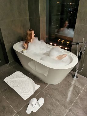 Kız pencerenin yanındaki köpük banyosunda banyo yapar ve dinlenir. Dinlenme ve rahatlama, spa tedavileri.