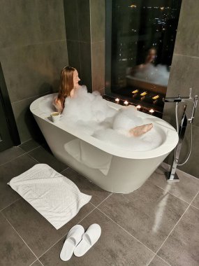 Kız pencerenin yanındaki köpük banyosunda banyo yapar ve dinlenir. Dinlenme ve rahatlama, spa tedavileri.