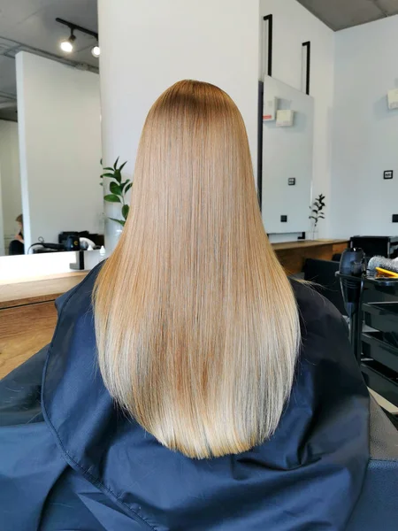 Beautiful long blond hair girl in a beauty salon after hair care. View from the back. Hairdresser styling concept.