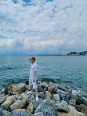 Adam Ege Denizi 'nin arka planında kayaların üzerinde duruyor ve bulutlu mavi gökyüzü. Kusadasi, Türkiye