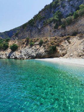 Gök mavisi kıyı manzarası, kayalar, çam ağaçları ve beyaz kum. Ege Denizi. Türkiye, Kusadasi