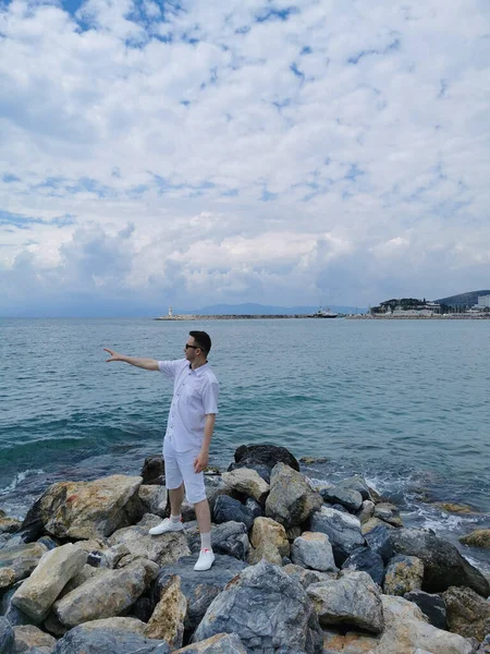 Voyageur Guy se tient sur les rochers sur le fond de la mer Égée et le ciel bleu avec des nuages. Kusadasi, Turquie. — Photo