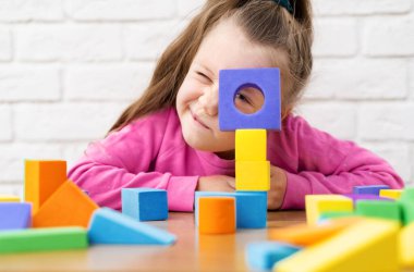 Küçük beyaz bir sarışın odada oynuyor, renkli küplerle dolu bir masada oturuyor. 5-6-7 yaşlarında bir çocuk çukura düştü.