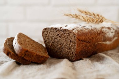 Bir somun ev yapımı koyu kokulu taze ekmek tahta bir tahtanın üzerinde dilimlenmiş ekmekle buğday kulaklı beyaz tuğla bir duvara karşı. Kır evi pişirme konsepti.