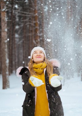 Çekici, beyaz tenli sarışın kadın kışın çam ormanlarında kar atıyor. Kış ormanında eğlence. Kuzey ülkesinde Noel tatili.