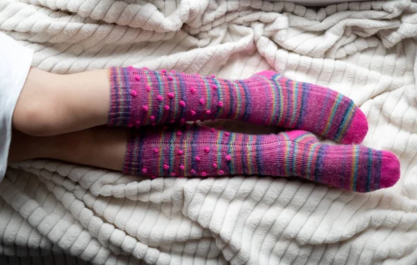 The legs of a young girl in lilac knitted socks-knee socks lying on a white soft bedspread. Cozy handmade knitted things