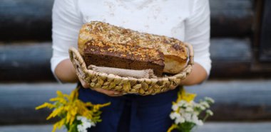 Baker 'ın elleri ahşap bir evin arka planına karşı ahşap bir sepette ev yapımı ekmek somunlarını tutuyordu. Mayasız buğday ve mayalı çavdar ekmeği. Aile pastanesi. Eko gıda konsepti