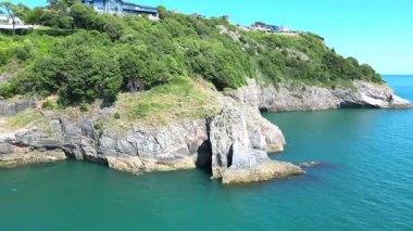 Torquay, Torbay, Devon, İngiltere: İHA arka planda Torquay kasabasını göstermeden önce Londra Kemeri olarak bilinen doğal özelliğin etrafında döner. Torbay, güzel kıyı şeridiyle ünlü popüler bir İngiliz tatil beldesidir..