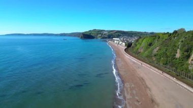 Teignmouth, Güney Devon, İngiltere: DRONE VİEWS: İnsansız hava aracı Teignmouth kasabasına ve binalarına ulaşmadan önce kumlu bir plaja paralel uçuyor. Teignmouth İngiltere 'nin popüler bir tatil beldesidir..