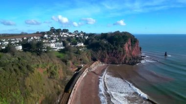 Teignmouth, Devon, İngiltere: DRONE VİEWS: İnsanlar Parson ve Clerk coğrafi özellikleri yakınlarındaki kıyı yolunda yürürken bir uçurum tünelinden yerel bir tren çıkıyor. Güney Devon, İngiltere 'nin popüler bir tatil beldesidir..